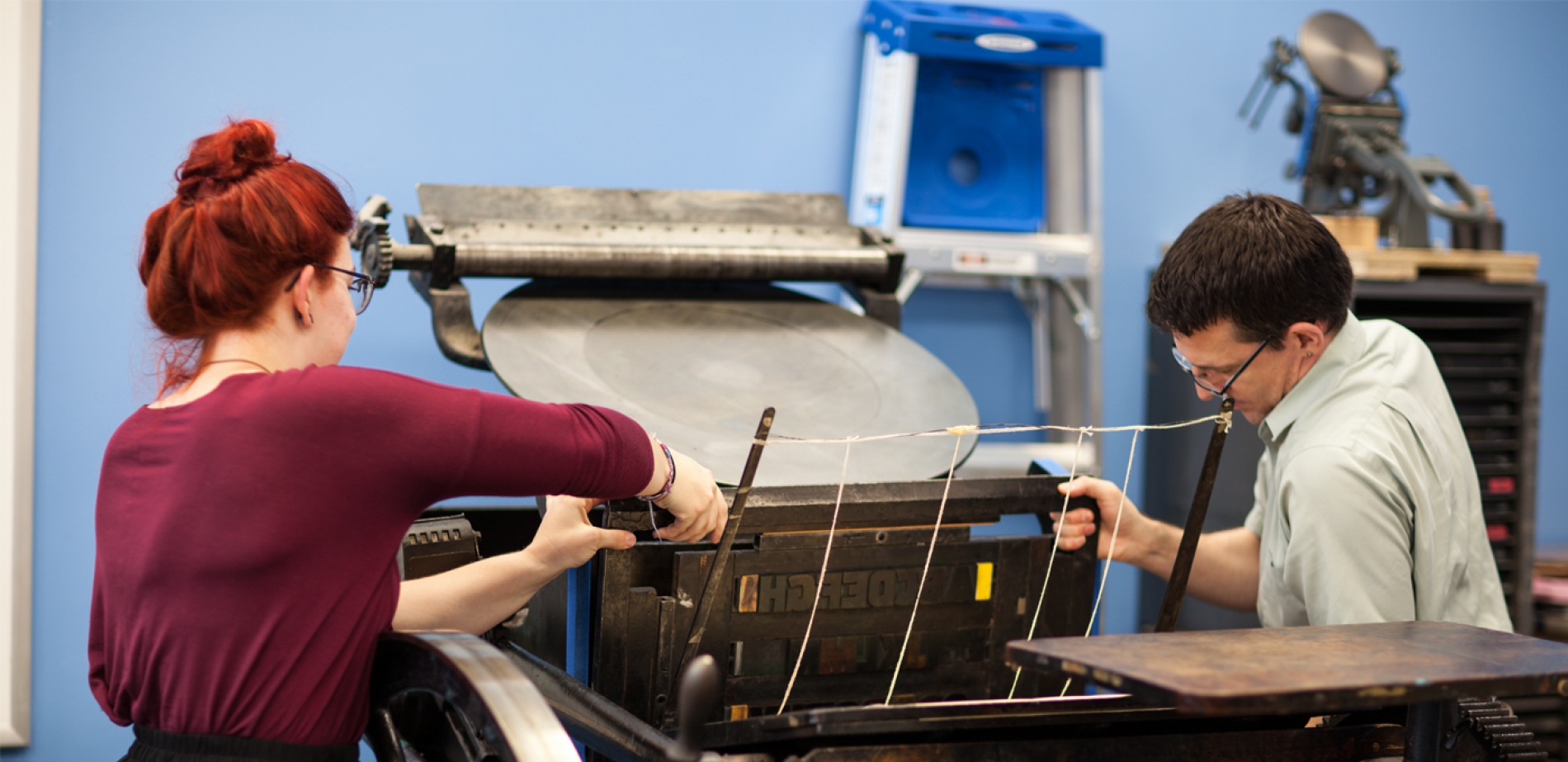 Faculty member Dr. Frech and a student work together to use an old-fashioned printing press.