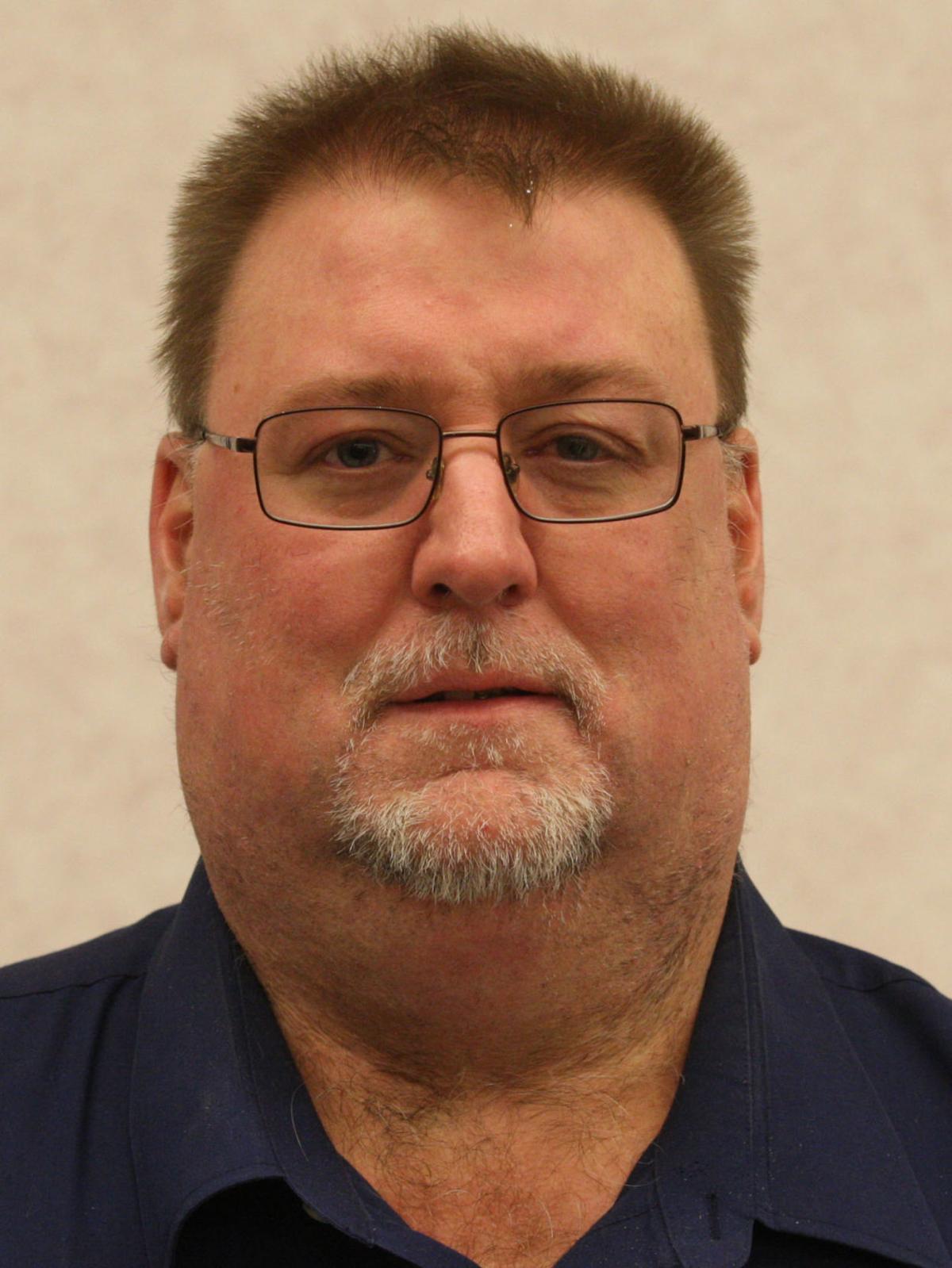 Dr. Scott Lambert, who is wearing a navy shirt with black glasses. He has light brown hair.